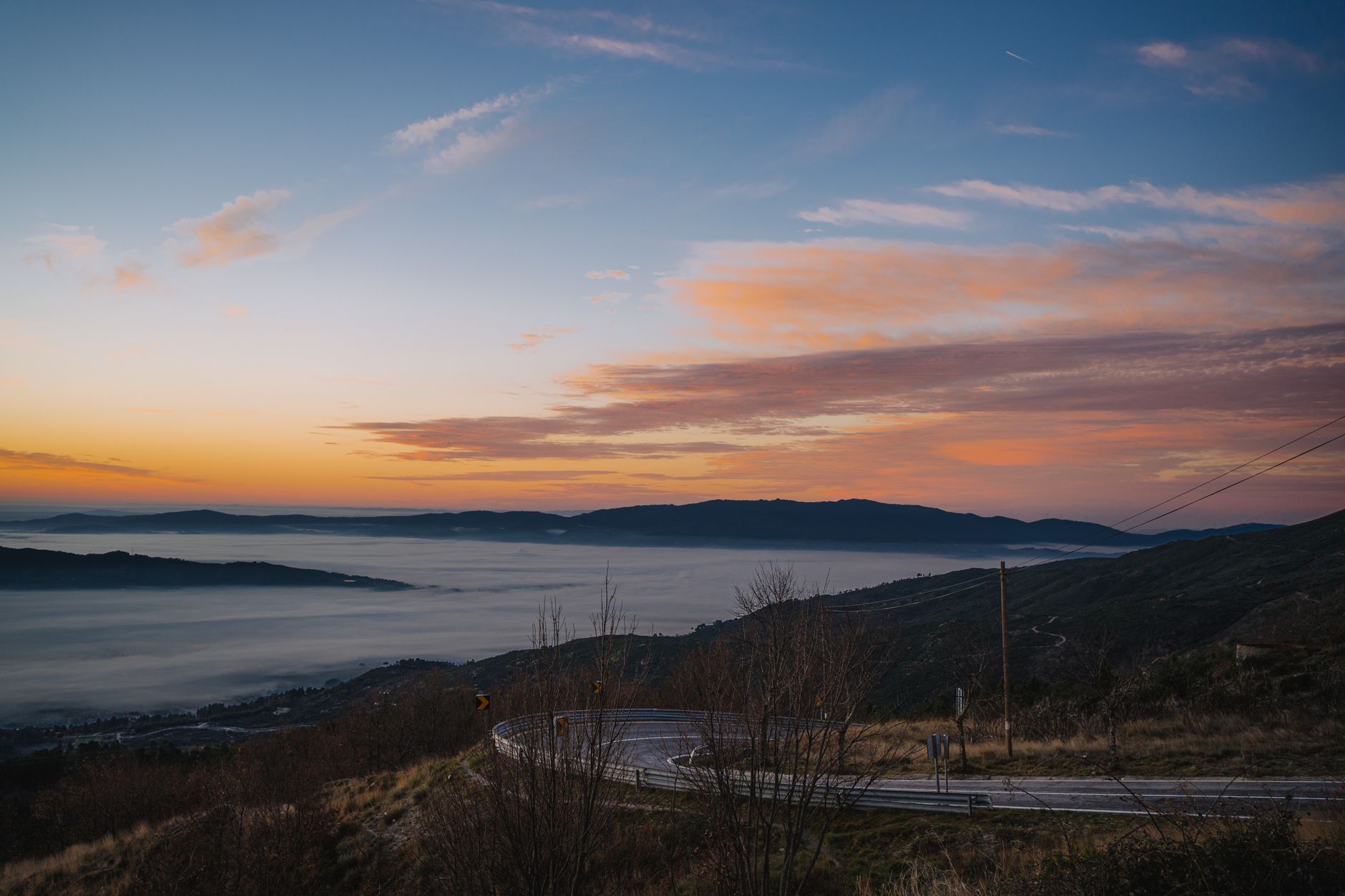 Breathtaking view of a mountain road at sunrise with foggy valleys and vibrant sky colors.