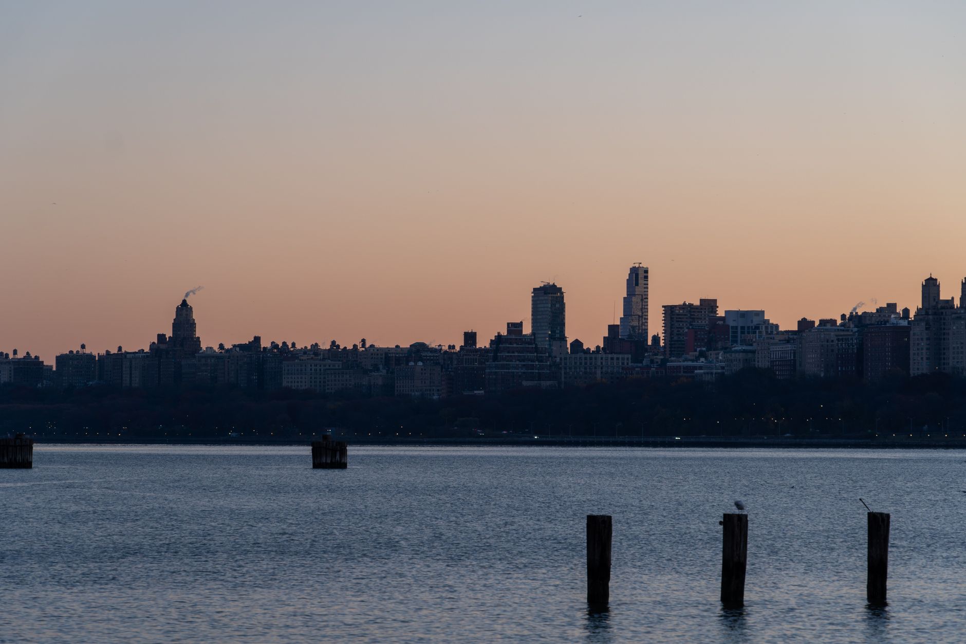 Capture of a city skyline at sunrise with calm waters in the foreground.